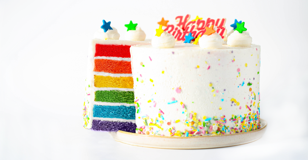 A rainbow cake that has been cut into, showing the vibrant coloured layers