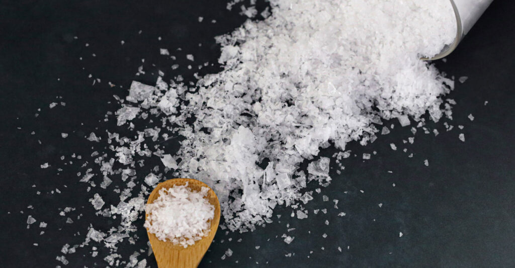 Salt falling out of a knocked over beaker with a wooden spoon representing sodium reduction