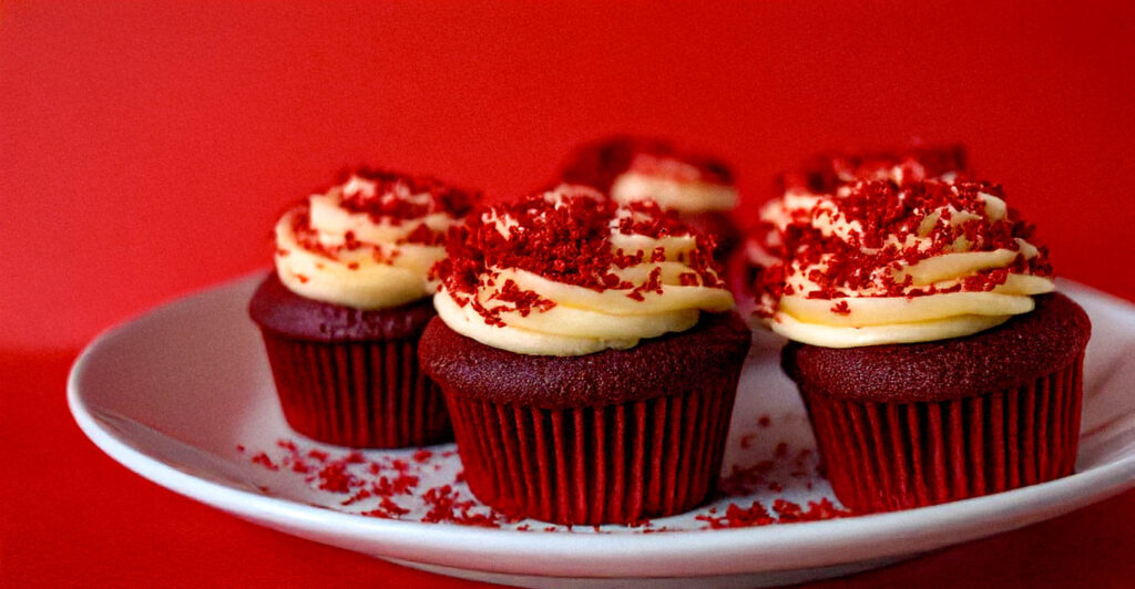 Plate of red velvet cupcakes and vanilla buttercream in swirls with a red backdrop