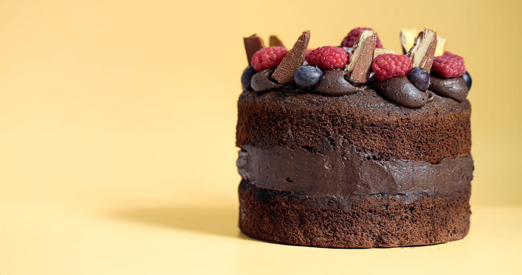 A chocolate celebration cake with chocolate icing and fresh berries with a plain yellow backdrop